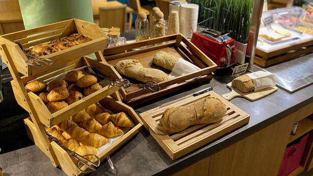 Un mostrador de buffet con diversos productos de panadería, incluyendo cruasanes y pan, presentados en bandejas de madera.