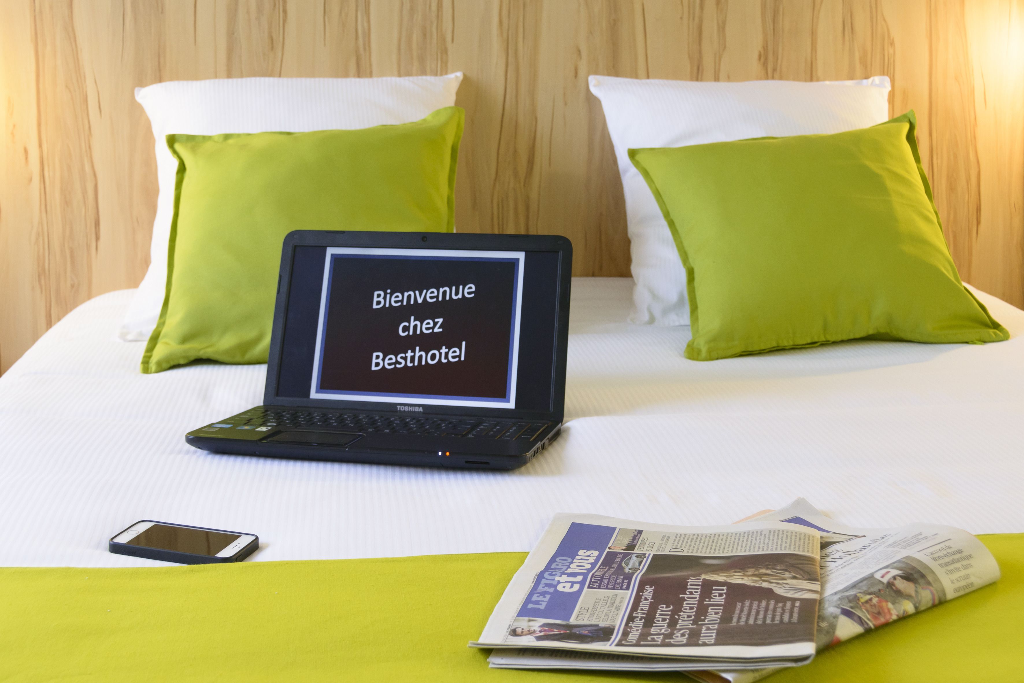 A laptop on a bed with a message on the screen, a smartphone, and a newspaper.