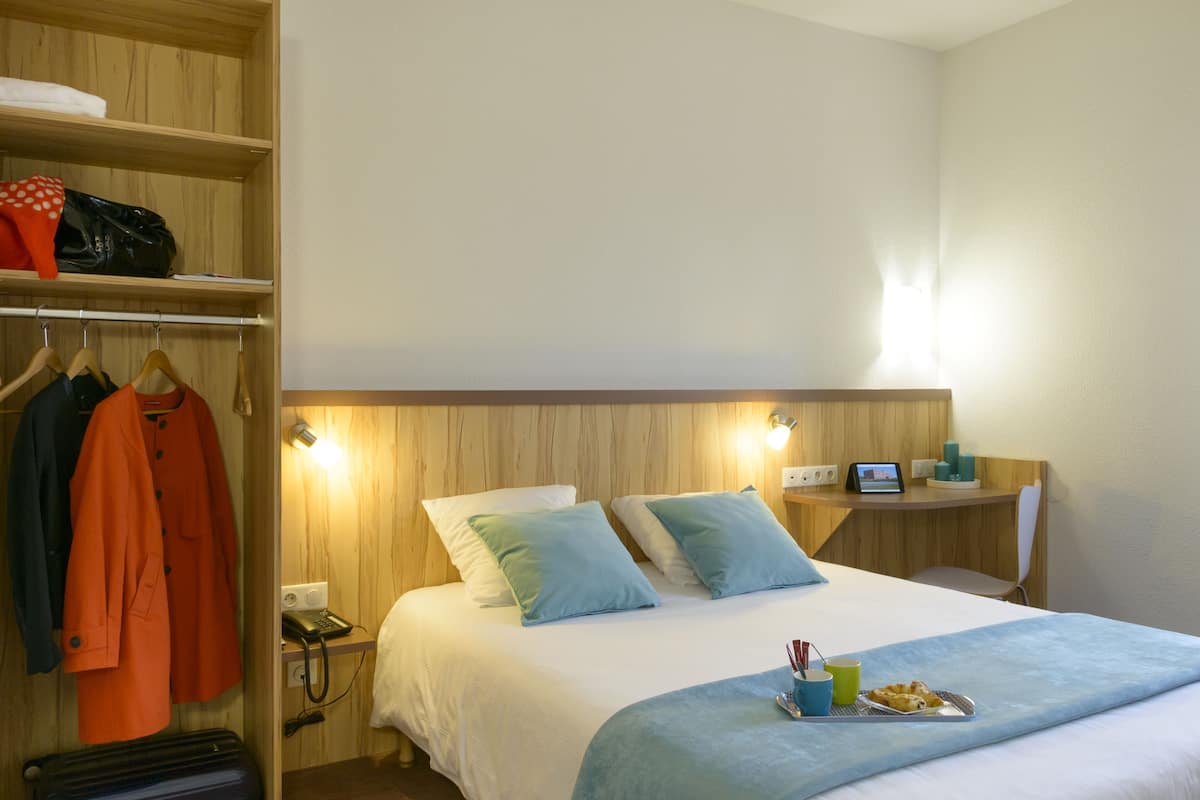 Ein Hotelzimmer mit einem Bett, einem Schreibtisch mit Computer, einem Stuhl, einem Kleiderschrank und einem Koffer.