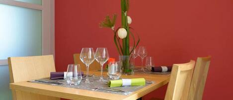 Una mesa de comedor preparada con copas de vino, un florero con una flor y un mantel individual verde.