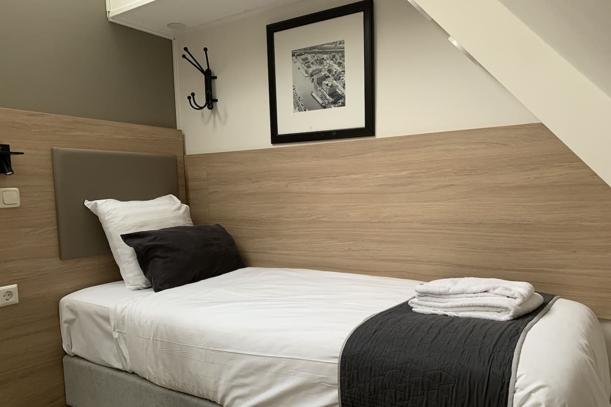 A neatly made bed with white and black bedding, a grey headboard, and a black quilted throw.