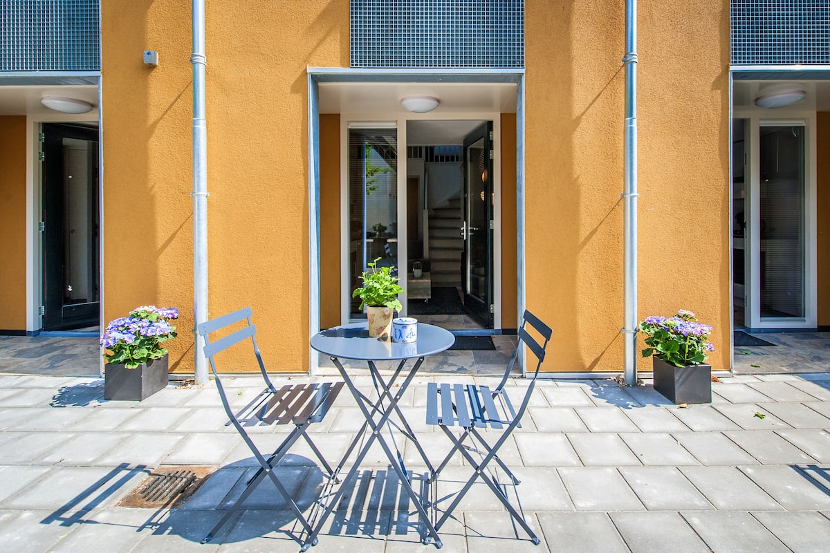 An outdoor seating area with a table and chairs, potted plants, and a building entrance.