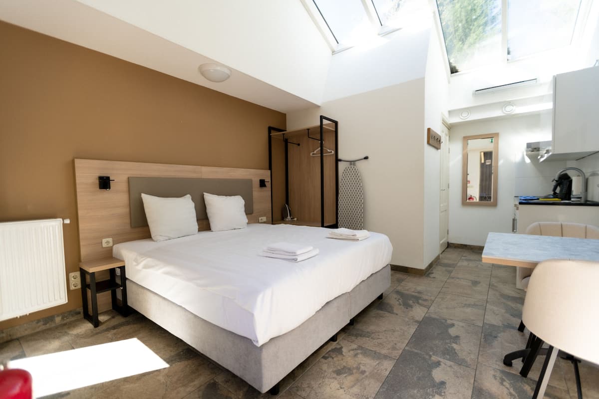 A modern hotel room with a large bed, a small table, and a kitchenette.
