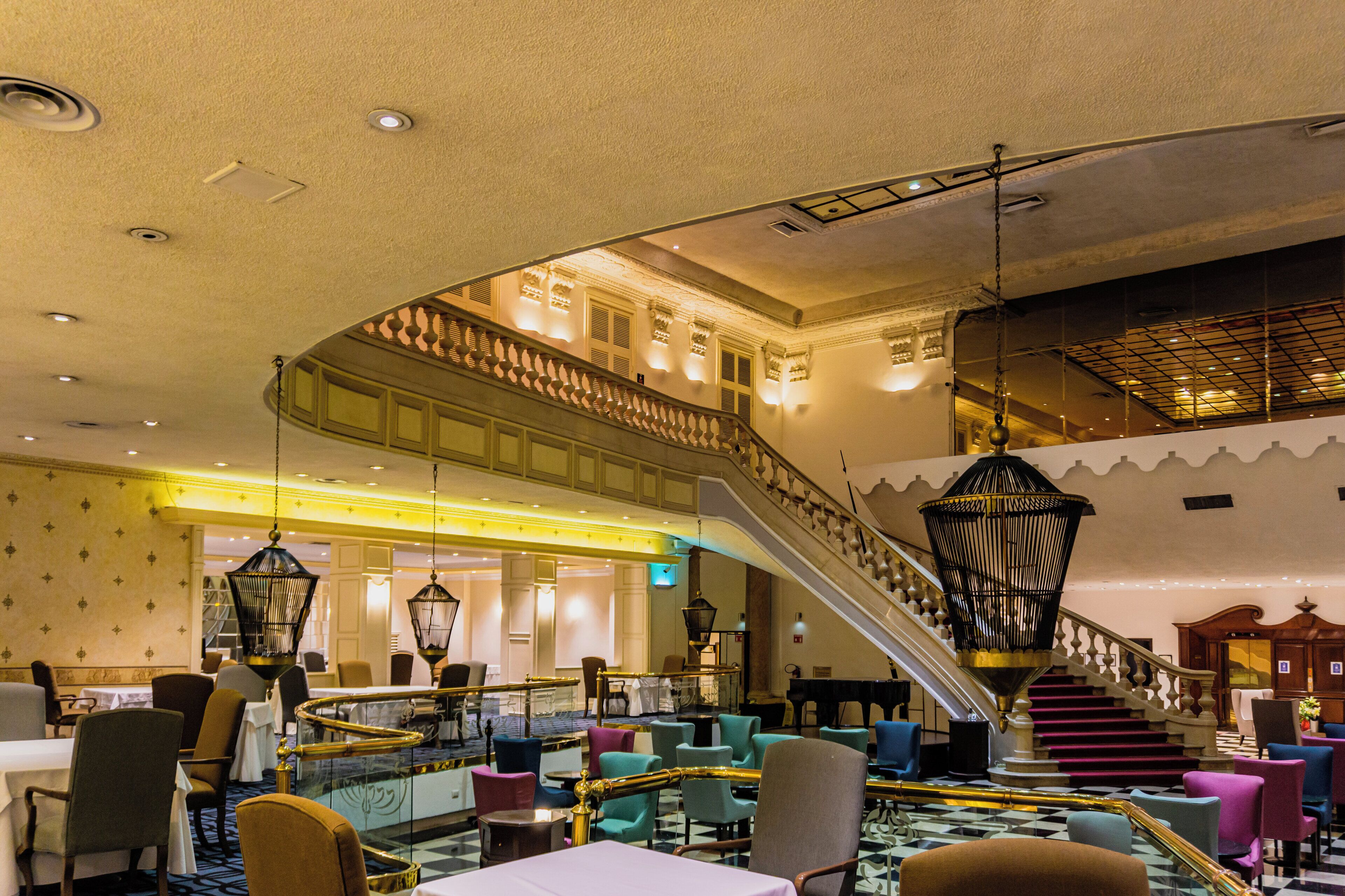 A spacious lobby with a grand staircase, multiple seating areas, and a piano.