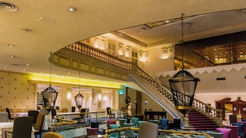 A spacious lobby with a grand staircase, multiple seating areas, and a piano.