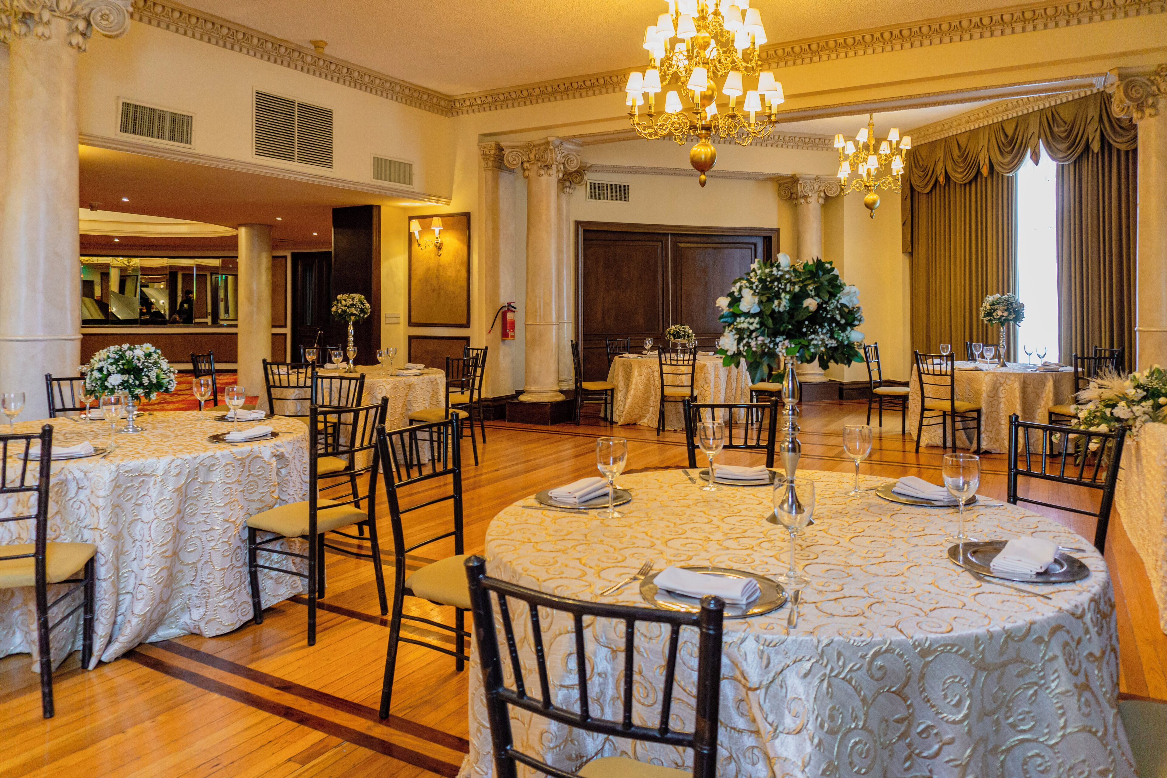 A formal dining room with round tables, chairs, and chandeliers.