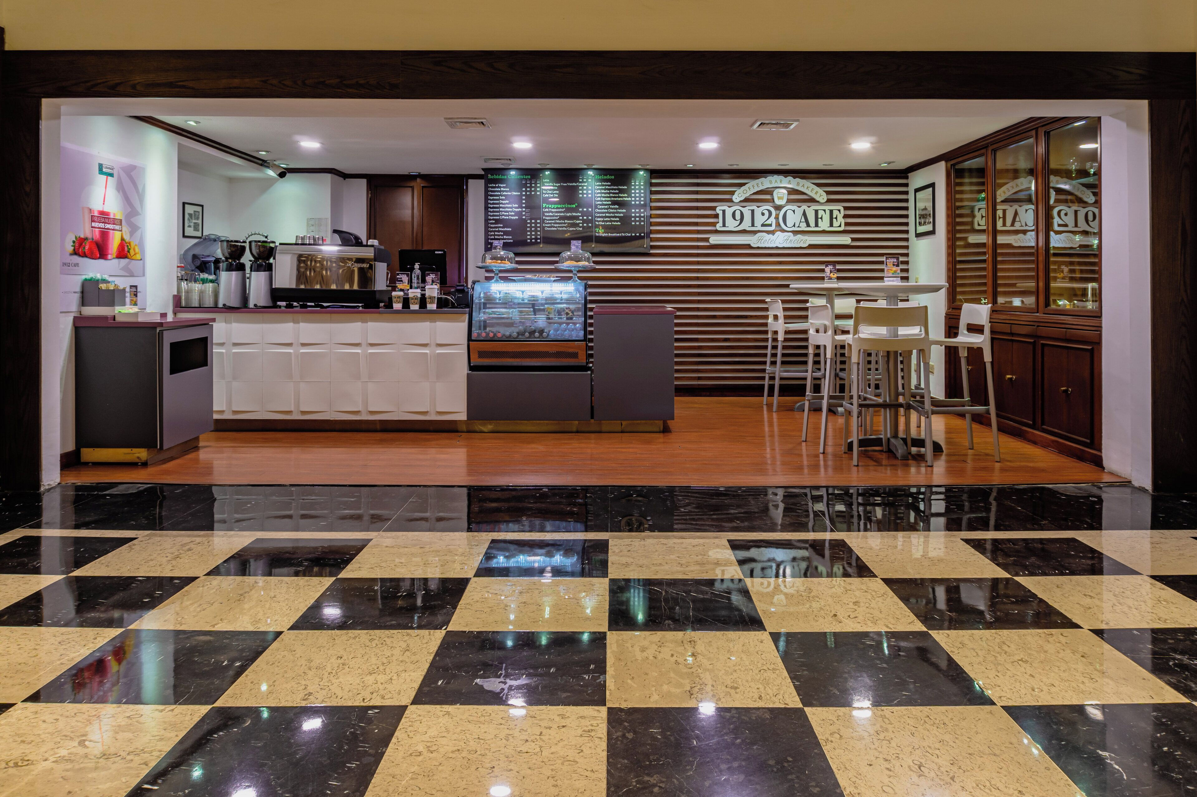 A modern coffee bar with a menu board, seating area, and a checkered floor.