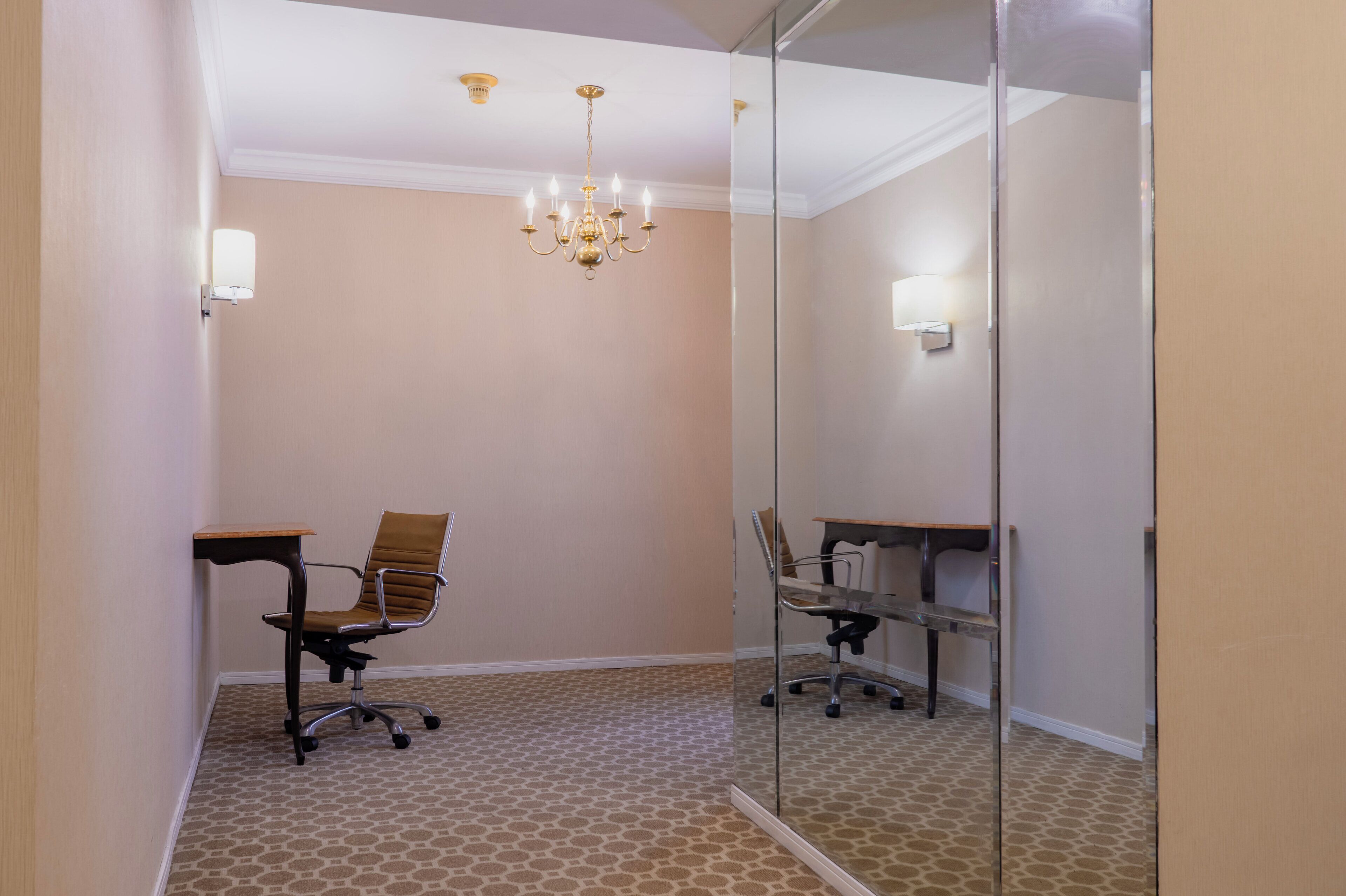 A small, well-lit room with a single office chair, a small table, and a chandelier.