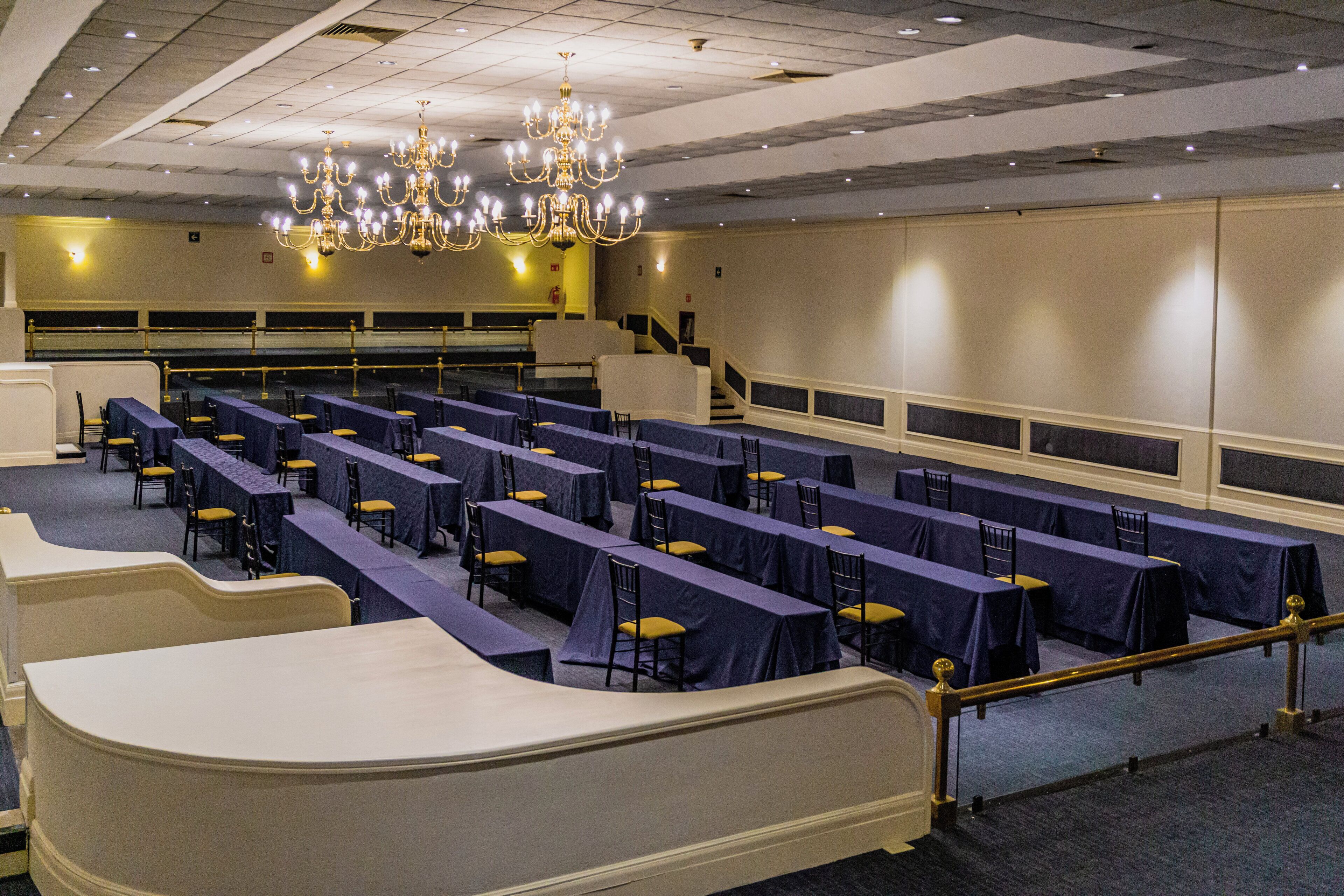 Un salón de conferencias con filas de mesas y sillas, una araña de cristal y una escalera.