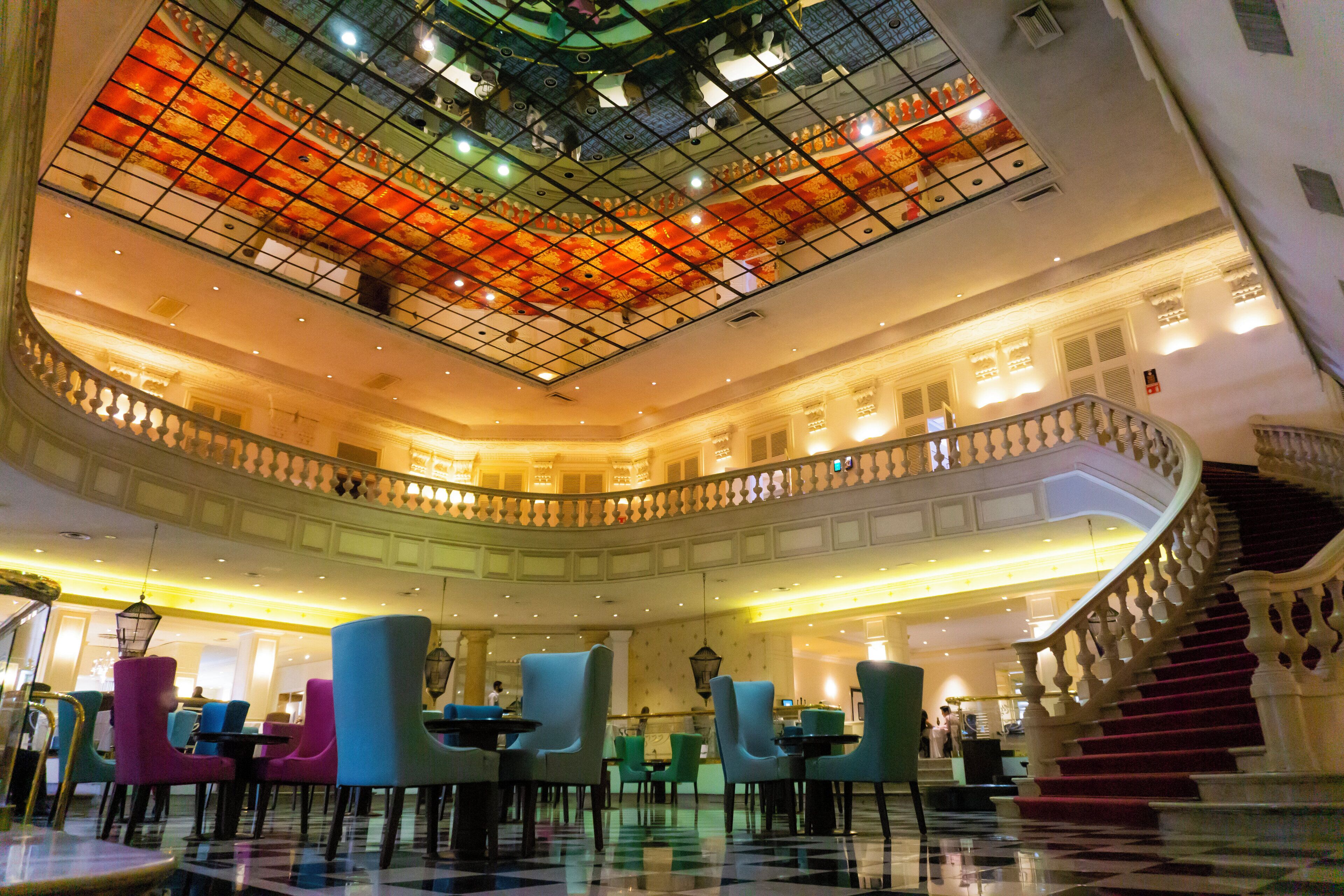 En hotellobby i flera våningar med en central innergård, en storslagen trappa och sittgrupper.