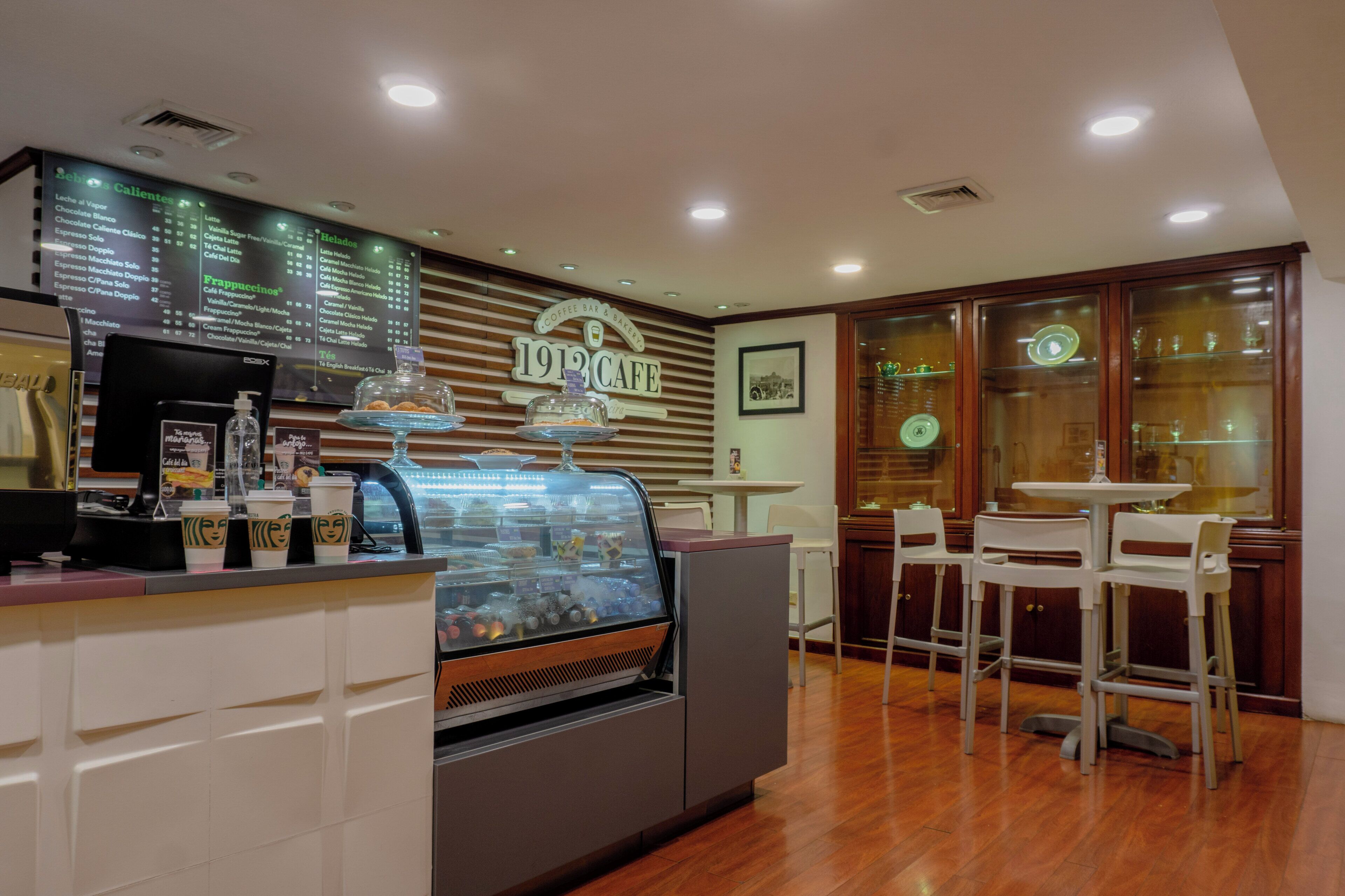 A cafe interior with a menu board, a coffee machine, a display case with desserts, and a seating area with tables and chairs.