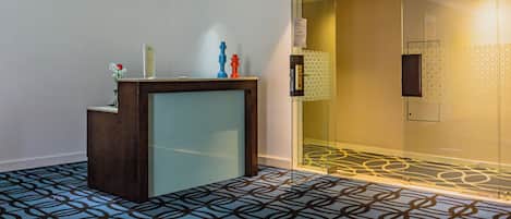 A reception area with a patterned carpet, a wooden reception desk, and a glass door leading to a room.