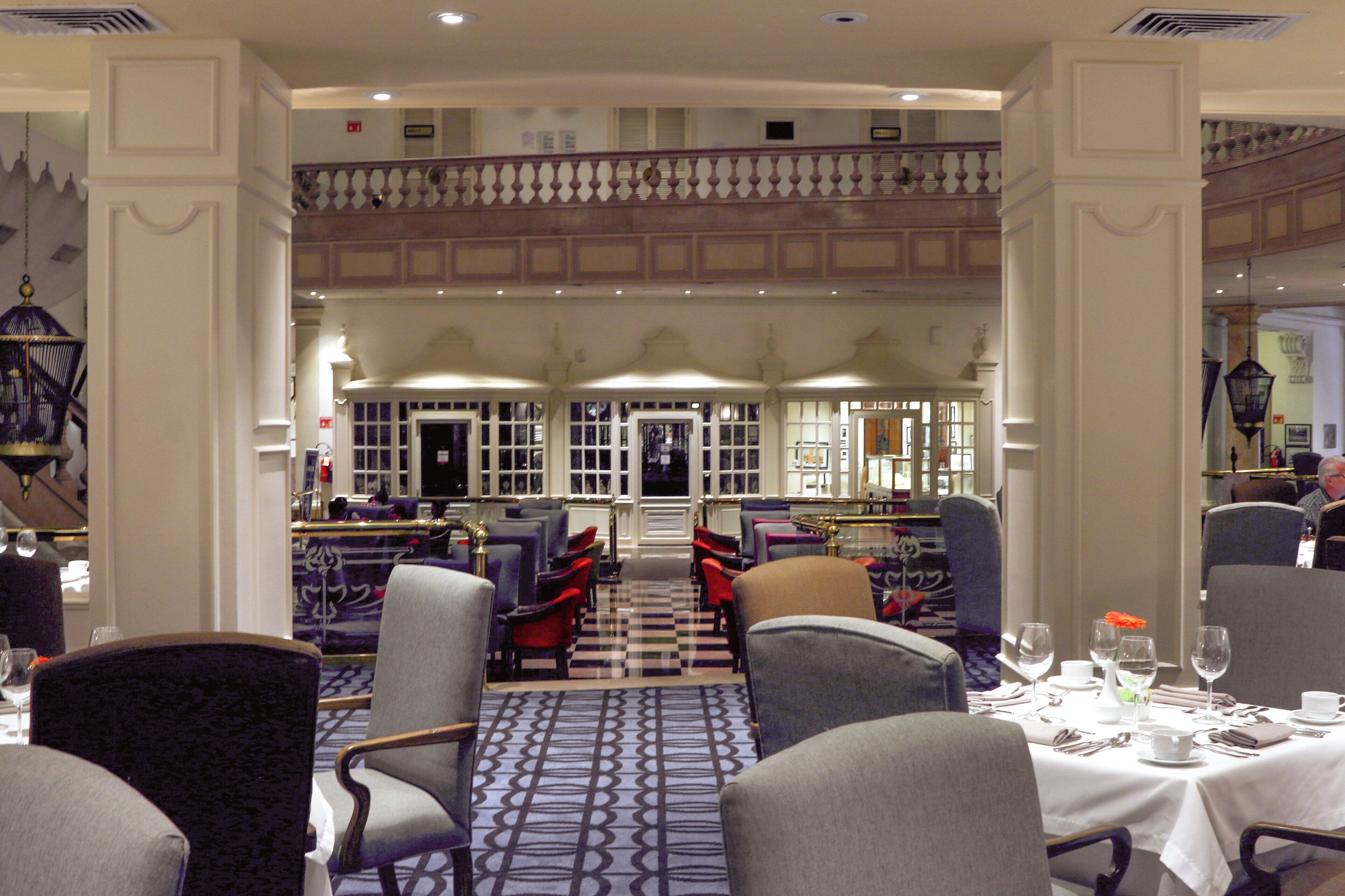 A hotel dining area with multiple tables set for guests, chairs arranged in rows, and a checkered floor pattern.