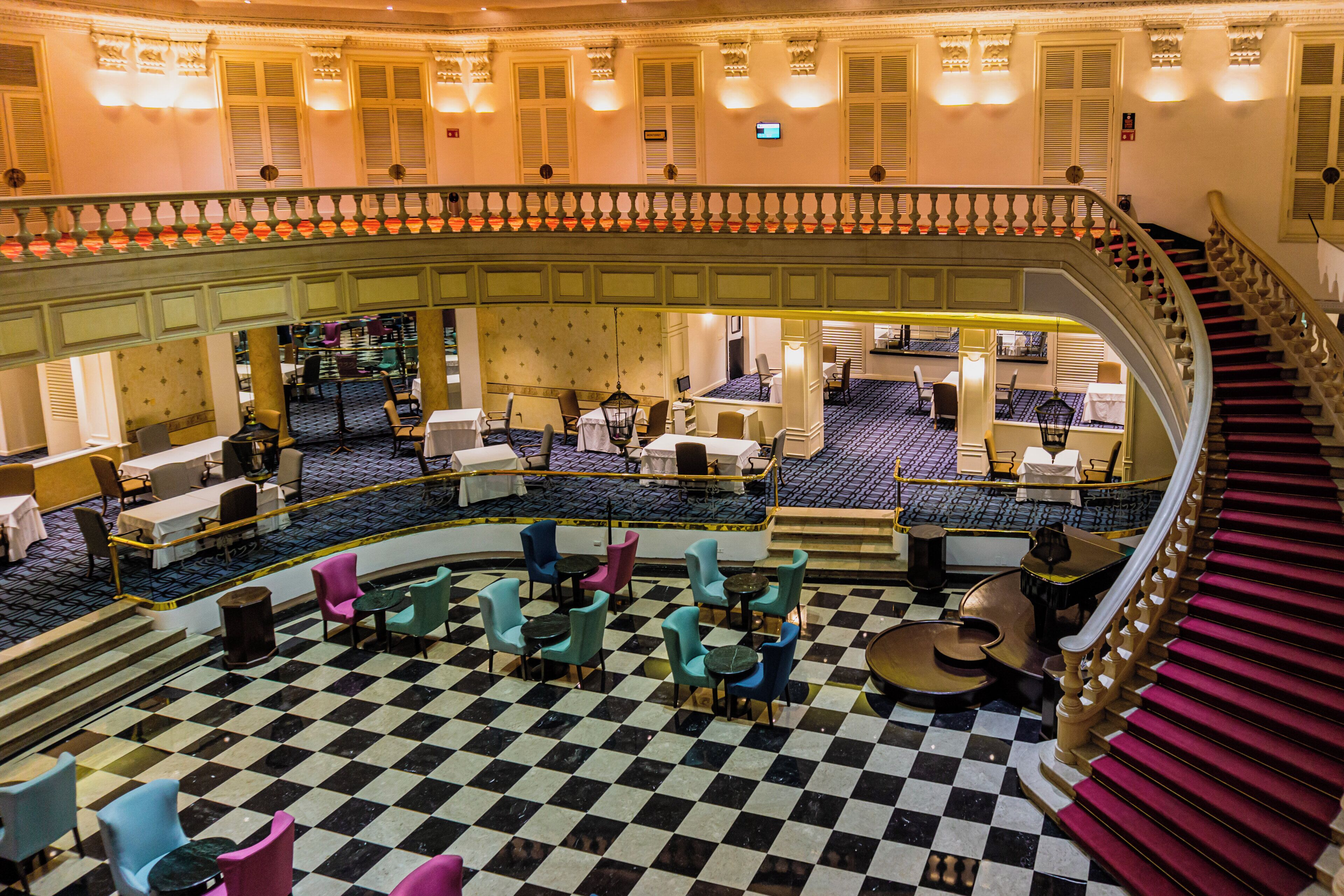 A hotel lobby with a checkered floor, multiple seating areas, and a grand staircase.