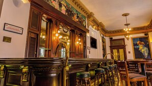 A bar area with wooden bar stools, a mirror, and a mural on the wall. - Gamma de Fiesta Americana Monterrey Gran Hotel Ancira (Monterrey)