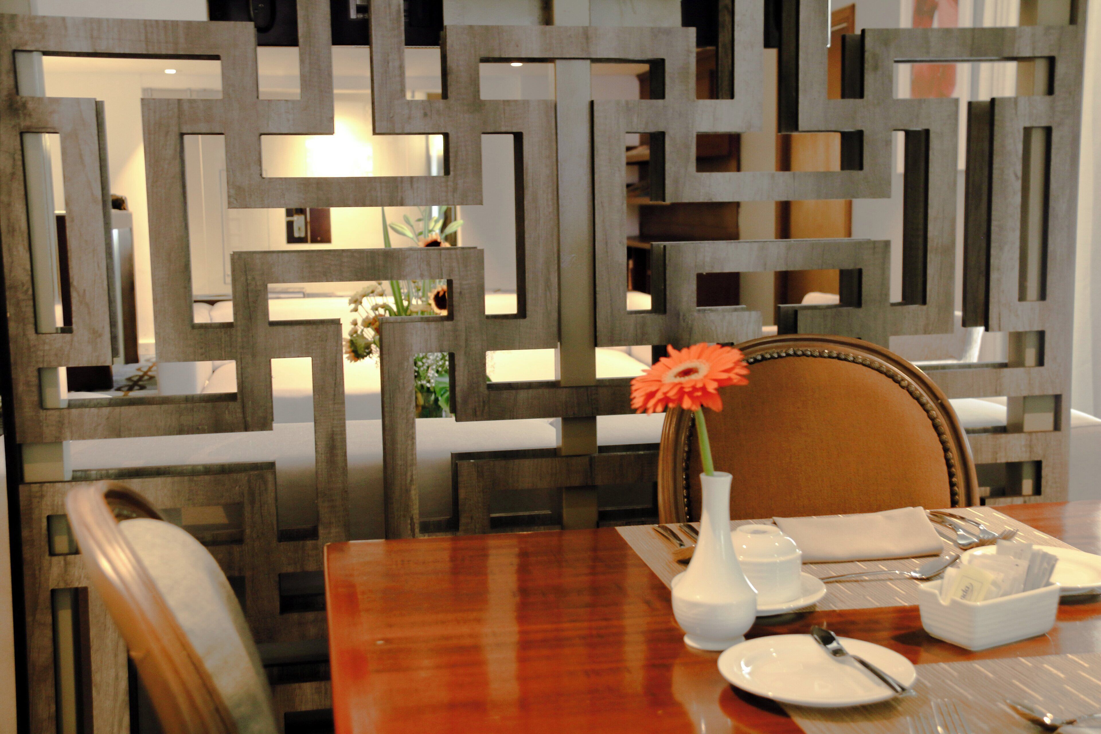 A dining table set with plates, cutlery, a vase with a flower, and a decorative wall panel in the background.