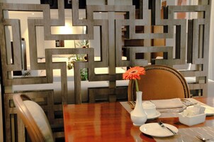 A dining table set with plates, cutlery, a vase with a flower, and a decorative wall panel in the background.