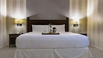 Una cama grande con cabecera de madera, dos mesitas de noche con lámparas, una bandeja con alimentos para el desayuno y un teléfono sobre la mesa de la izquierda.