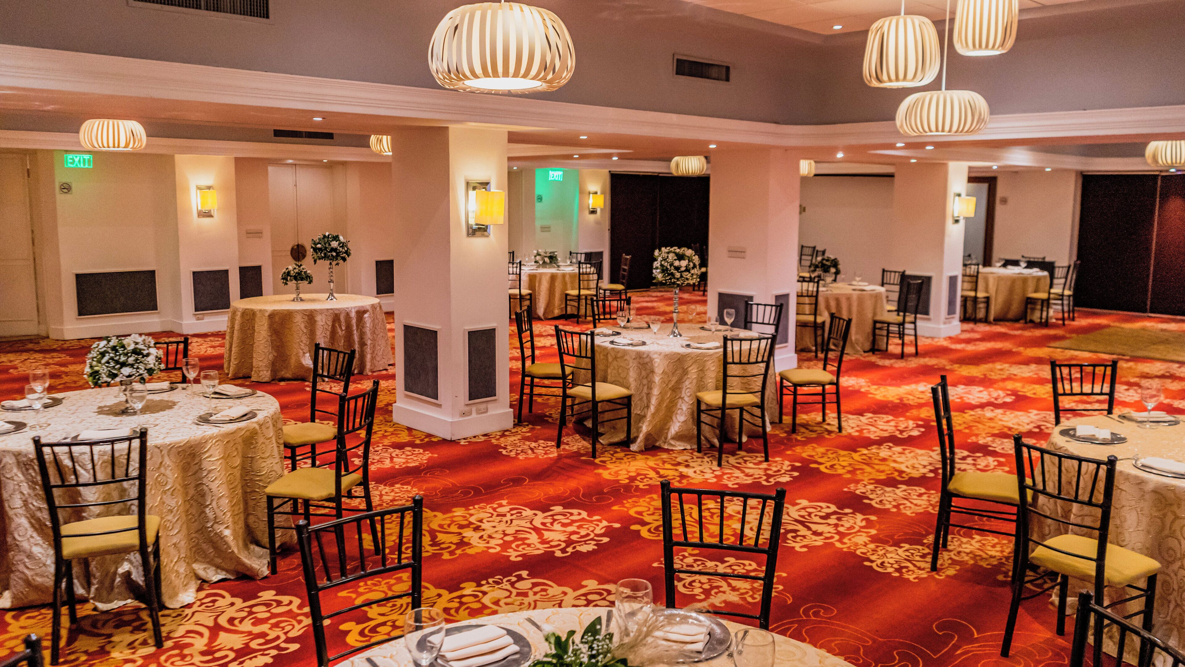 Un salón de banquetes con mesas redondas, sillas y piso cubierto de alfombra roja.