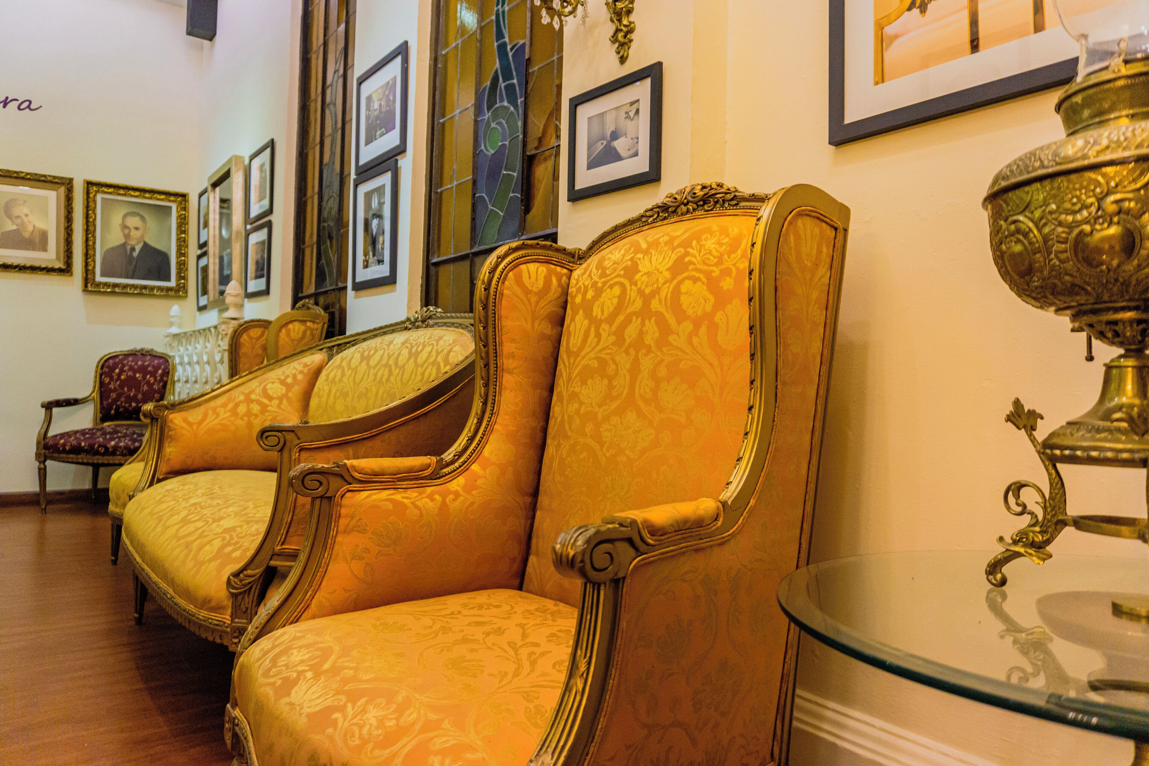 Um quarto com cadeiras douradas ricamente decoradas, uma mesa de vidro e quadros nas paredes.