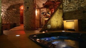 A stone-walled room with a wooden staircase leading to a wooden door. A hot tub is visible in the foreground. - Hotel Tivet (Gressan)