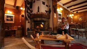 A cozy room with a stone fireplace, wooden furniture, and a rustic decor. - Hotel Tivet (Gressan)