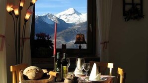 A dining table with a loaf of bread, wine bottles, glasses, and a candle, set against a window with a mountain view. - Hotel Tivet (Gressan)