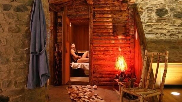 A rustic wooden cabin with a stone wall, a fire, and a wooden chair. - Hotel Tivet (Gressan)