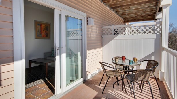 Une terrasse couverte avec une table et des chaises, une porte-fenêtre coulissante et une clôture blanche.