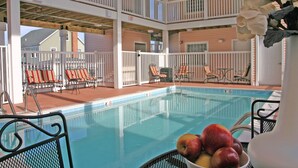 Un espace piscine avec vue sur un immeuble de deux étages, des chaises longues et un saladier rempli de fruits.