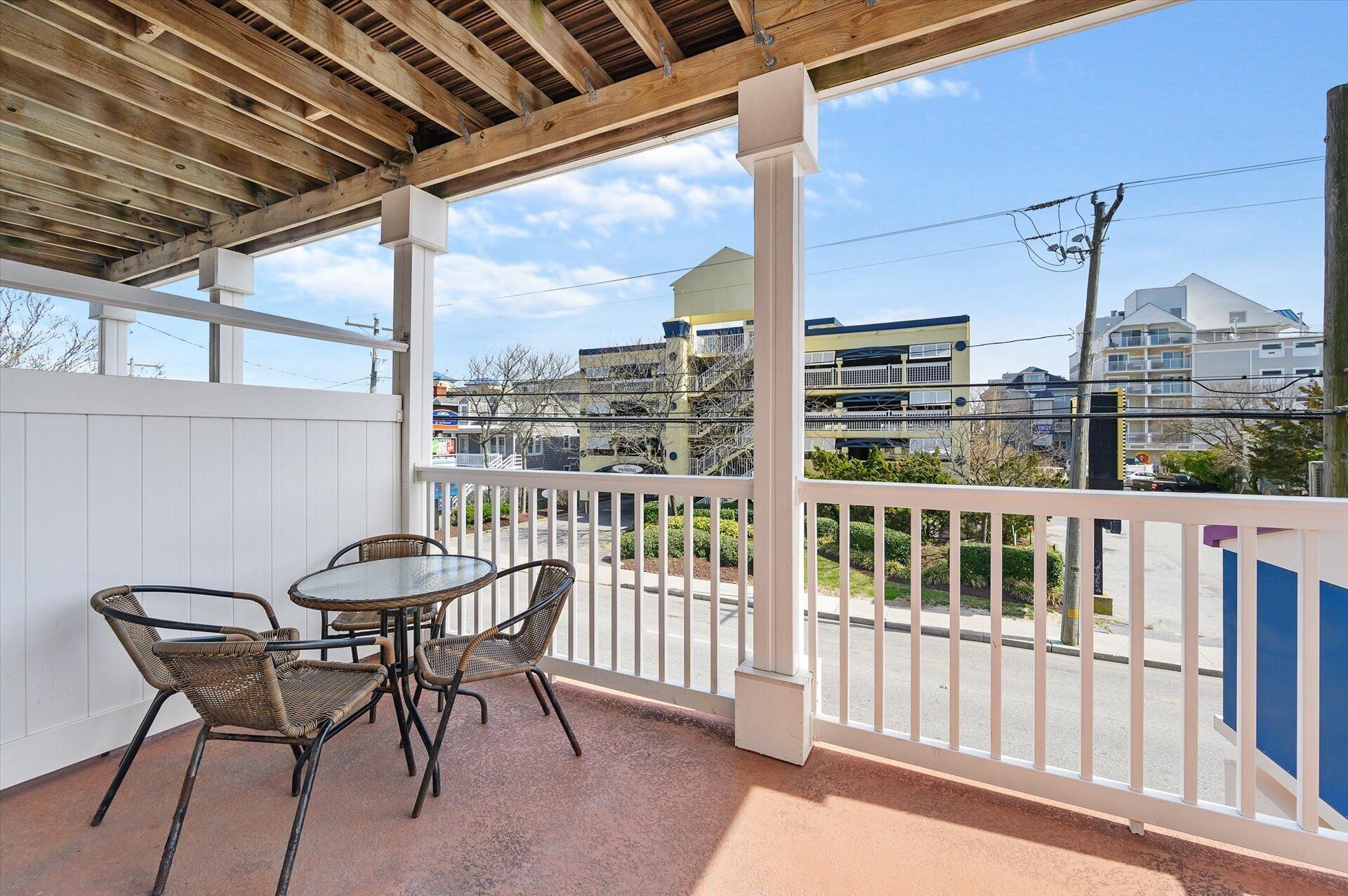 A covered patio with a table and chairs, overlooking a street with buildings and power lines.