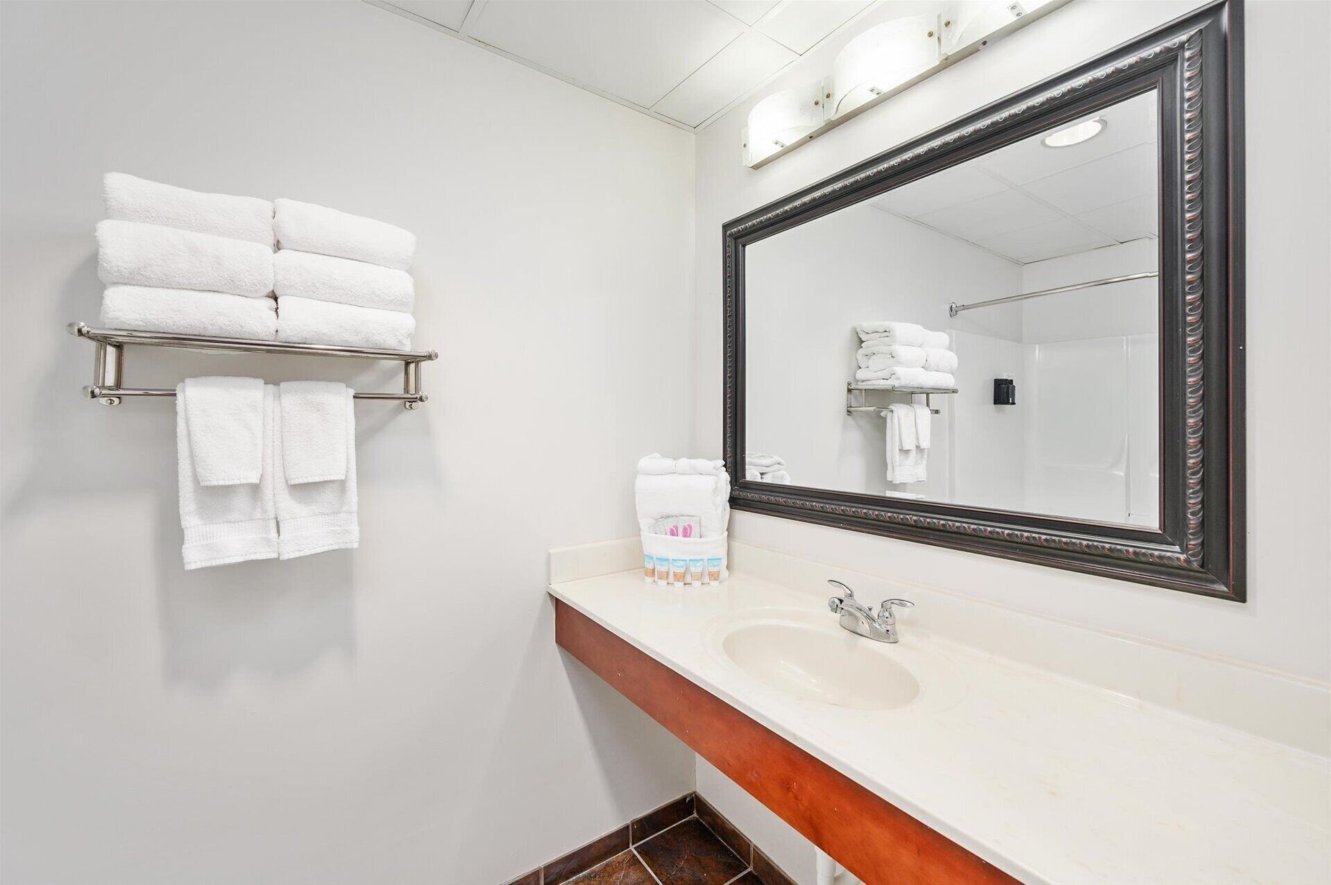 A bathroom with a white sink, a large mirror, and a towel rack with several white towels.