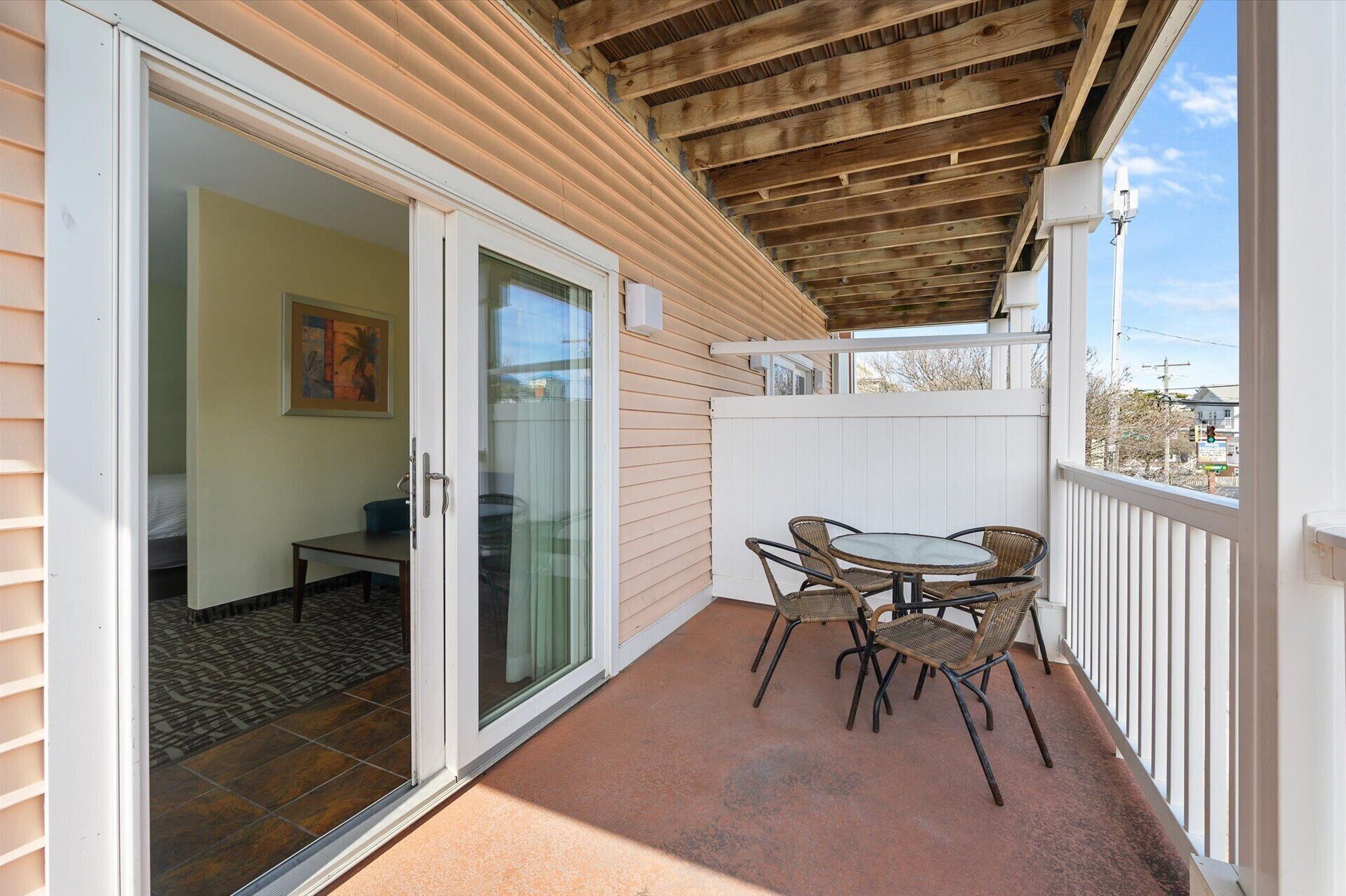 A covered patio with a table and chairs, a sliding glass door leading to an interior room, and a white fence surrounding the area.