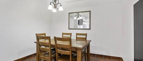 A dining area with a wooden table and chairs, a hanging light fixture, and a mirror on the wall.