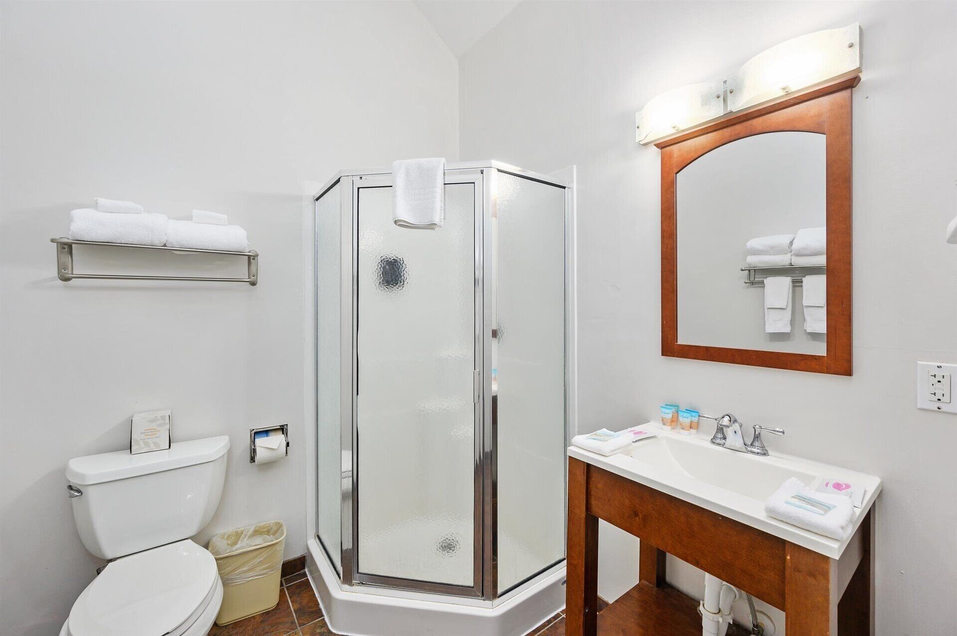 A modern bathroom with a glass-enclosed shower, a white sink with a wooden vanity, and a mirror above the sink.