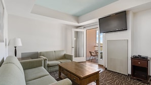 Un salon comprenant un canapé, une table basse, un téléviseur fixé au mur et une porte donnant sur un espace extérieur.