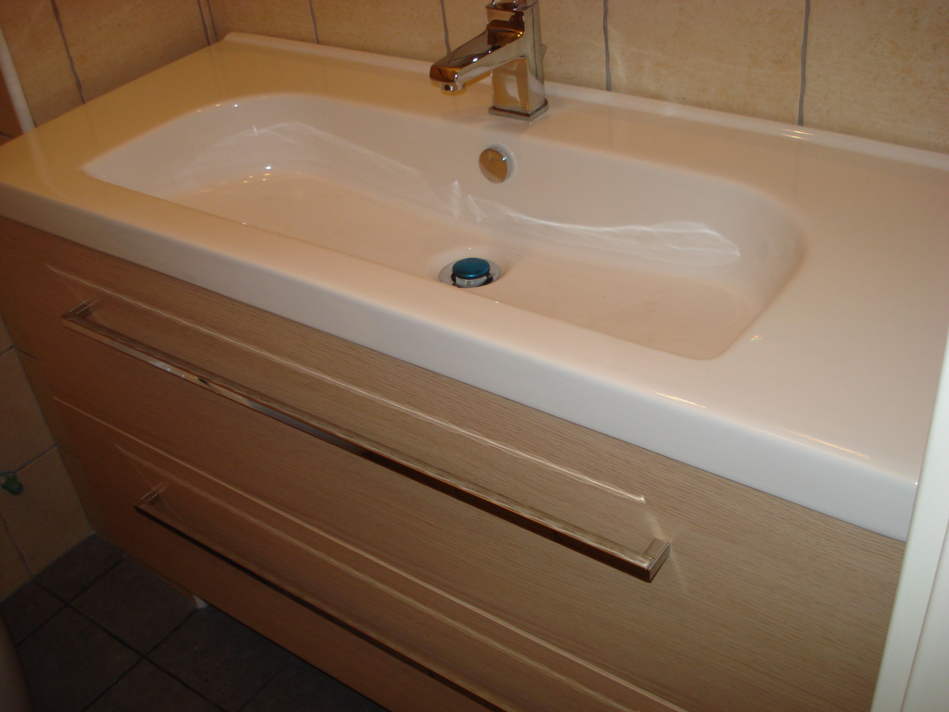 Un baño con un lavabo blanco, un mueble de madera debajo y una pared con azulejos.