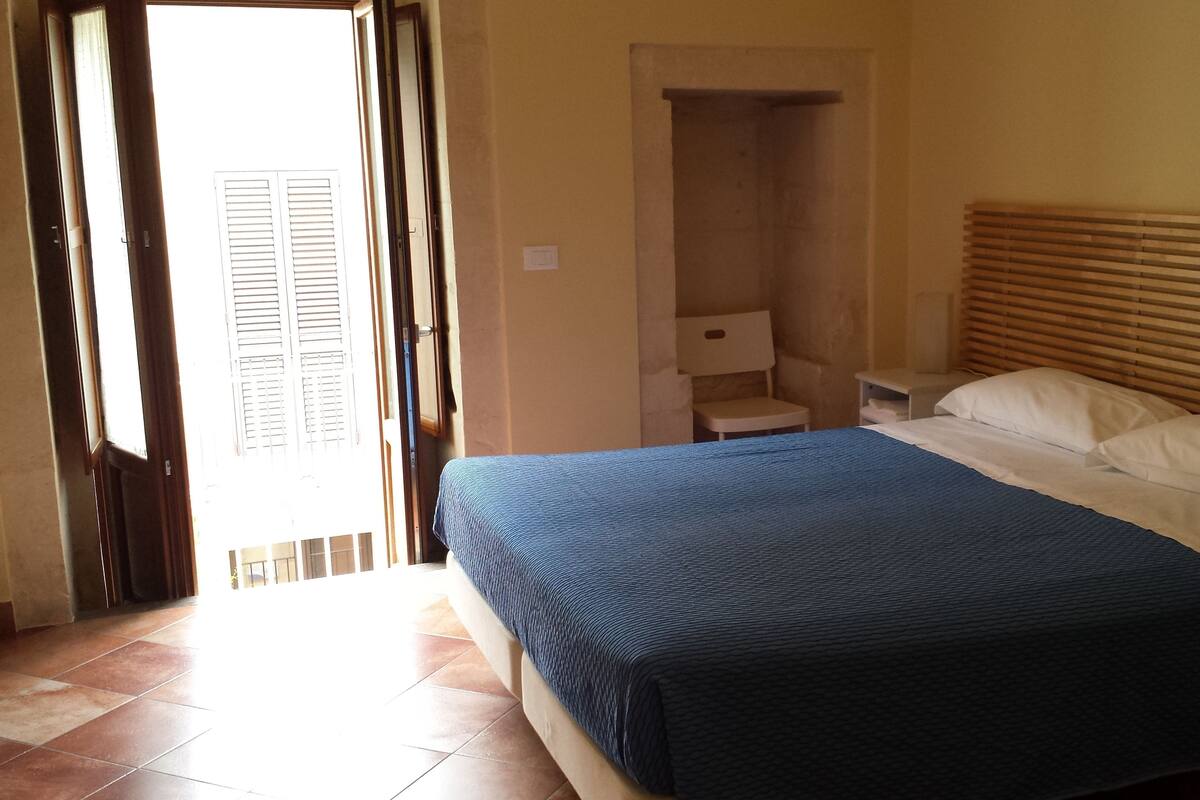 A bedroom with a bed, a nightstand, a chair, and a door leading to an outdoor area.