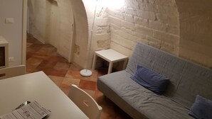 A cozy room with a stone archway, a grey sofa with blue cushions, a small white table, and a white chair. - Iblea Paradise (Ragusa)