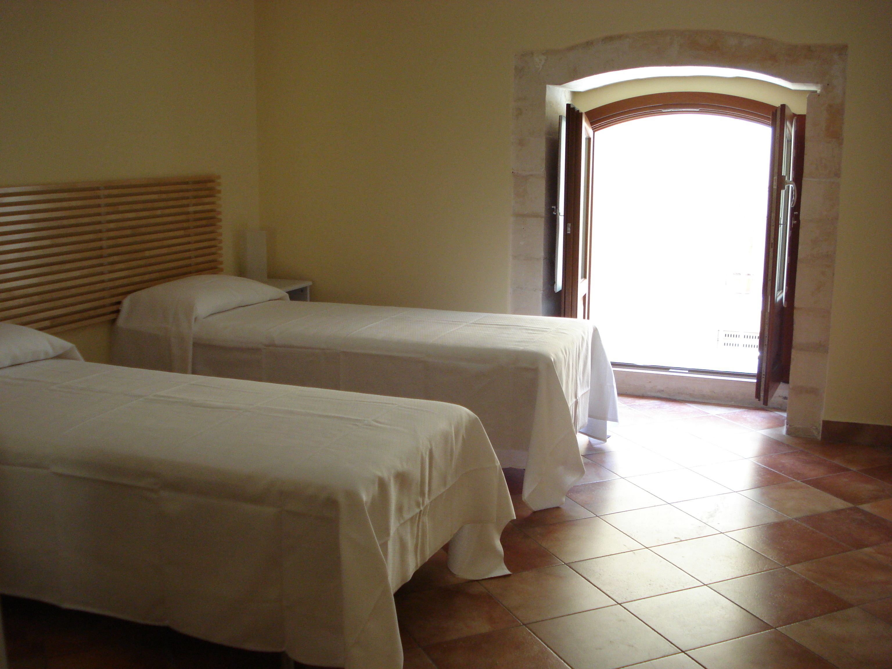 A room with two single beds, a wooden headboard, a small bedside table, and a tiled floor.