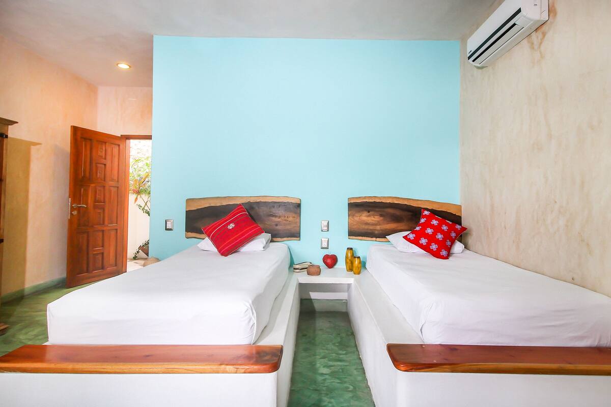 A room with two beds, a wooden door, and an air conditioning unit.
