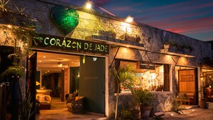 The exterior of the Hotel Corazon de Jade with a stone facade, potted plants, and a sign indicating a restaurant named "Aamal Home" inside. - Corazon de Jade Tulum Downtown (Tulum)