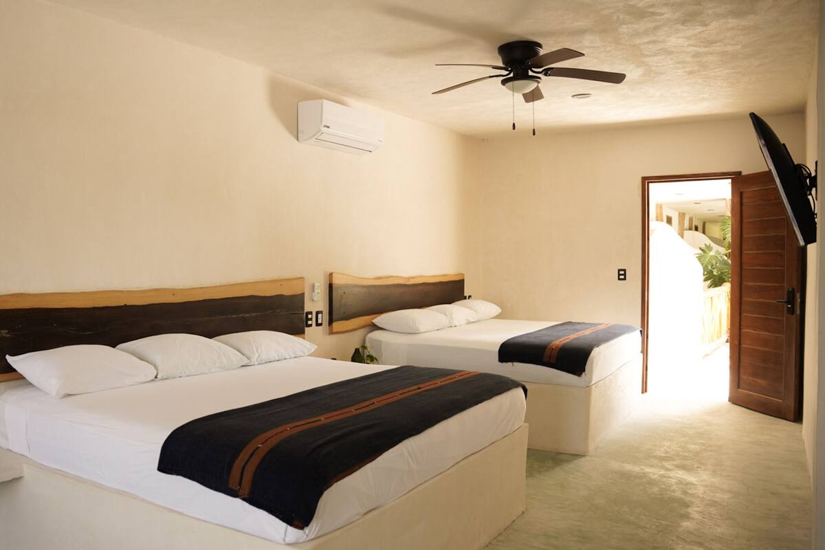 A hotel room with two beds, a ceiling fan, an air conditioning unit, and a door leading to an outdoor area.