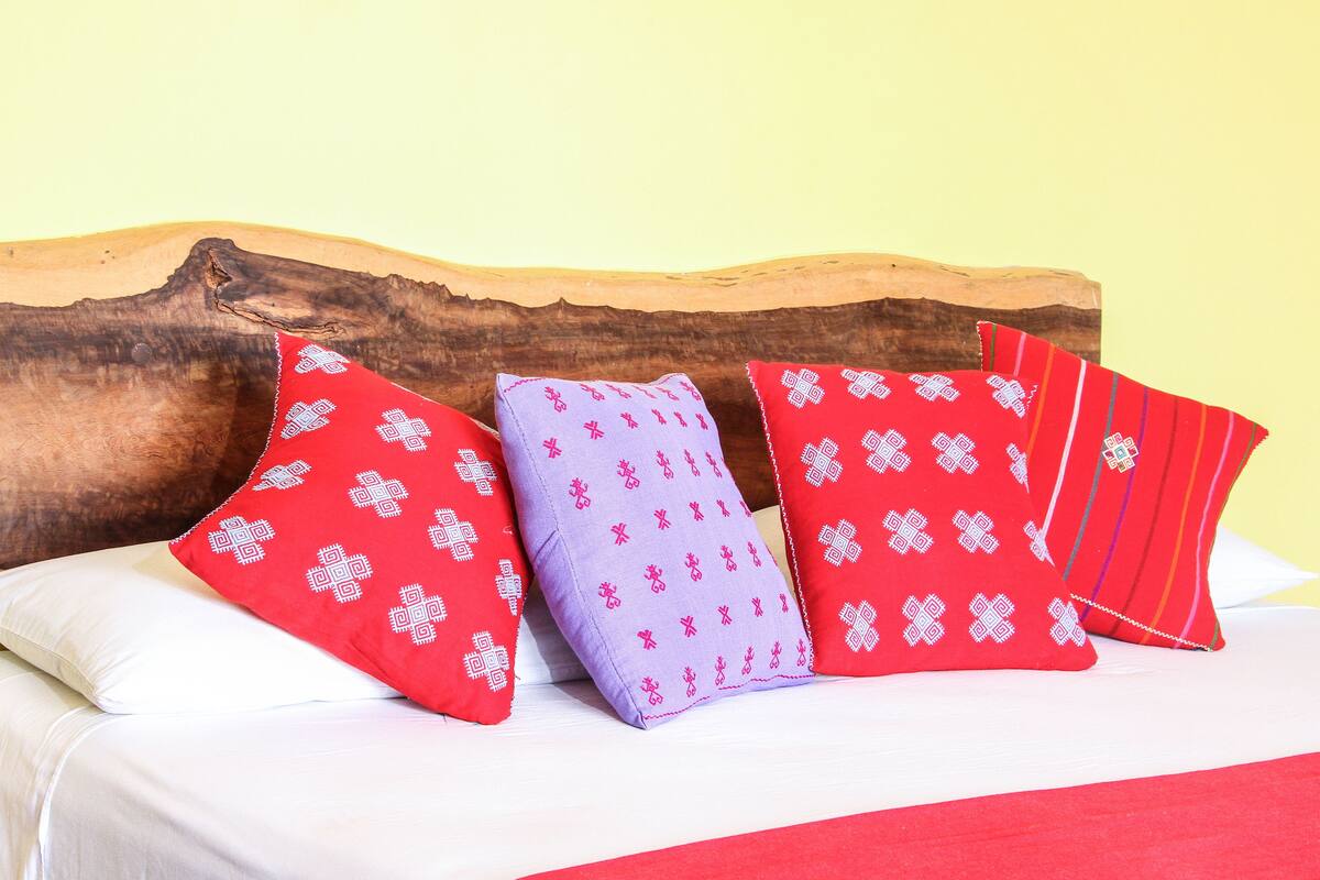 A bed with four pillows in different colors and patterns, a wooden headboard, and a plain yellow wall.