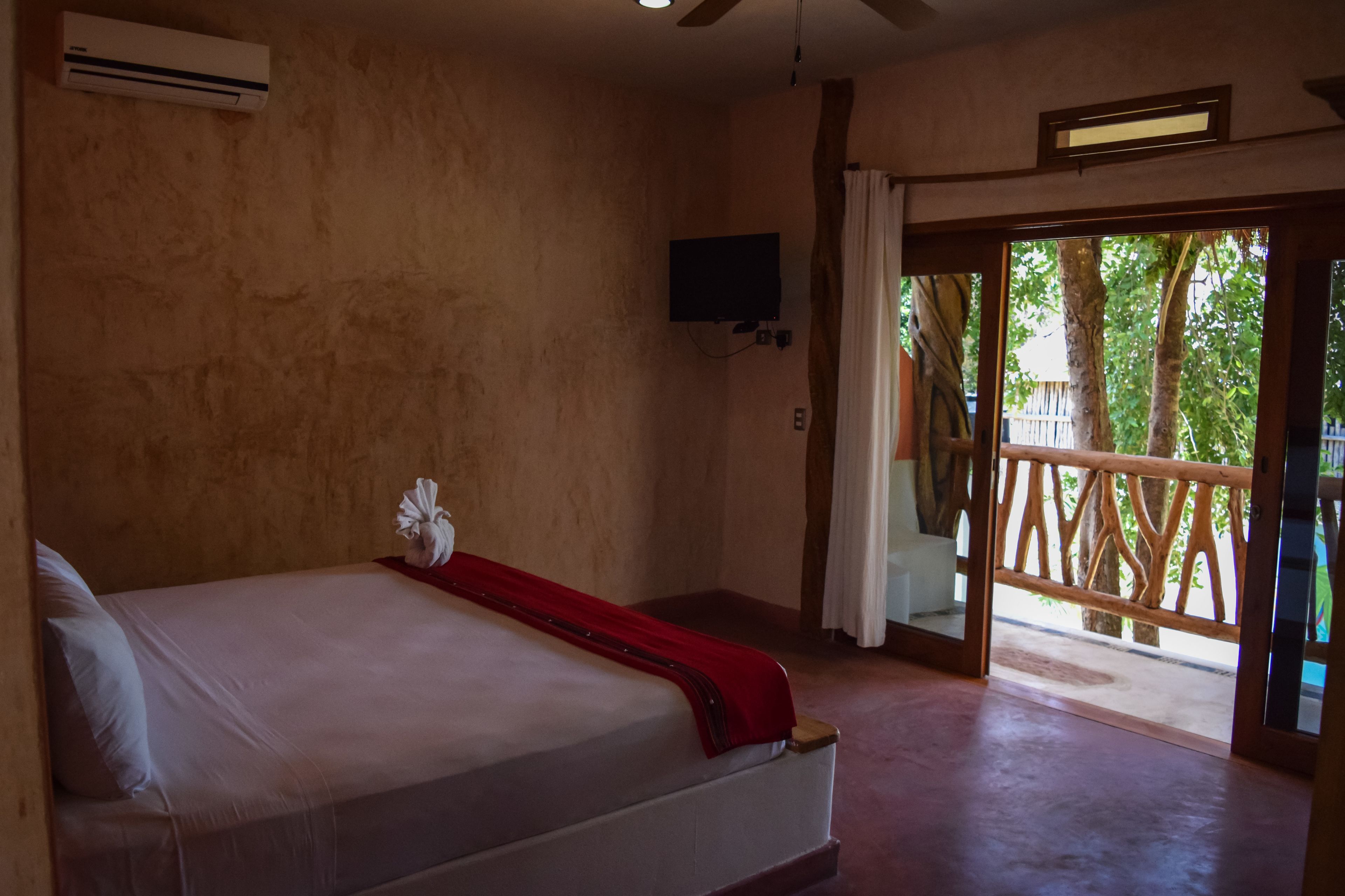 Une chambre d’hôtel équipée d’un lit, d’un appareil de climatisation, d’une télévision et offrant une vue sur l’extérieur grâce à une porte coulissante.