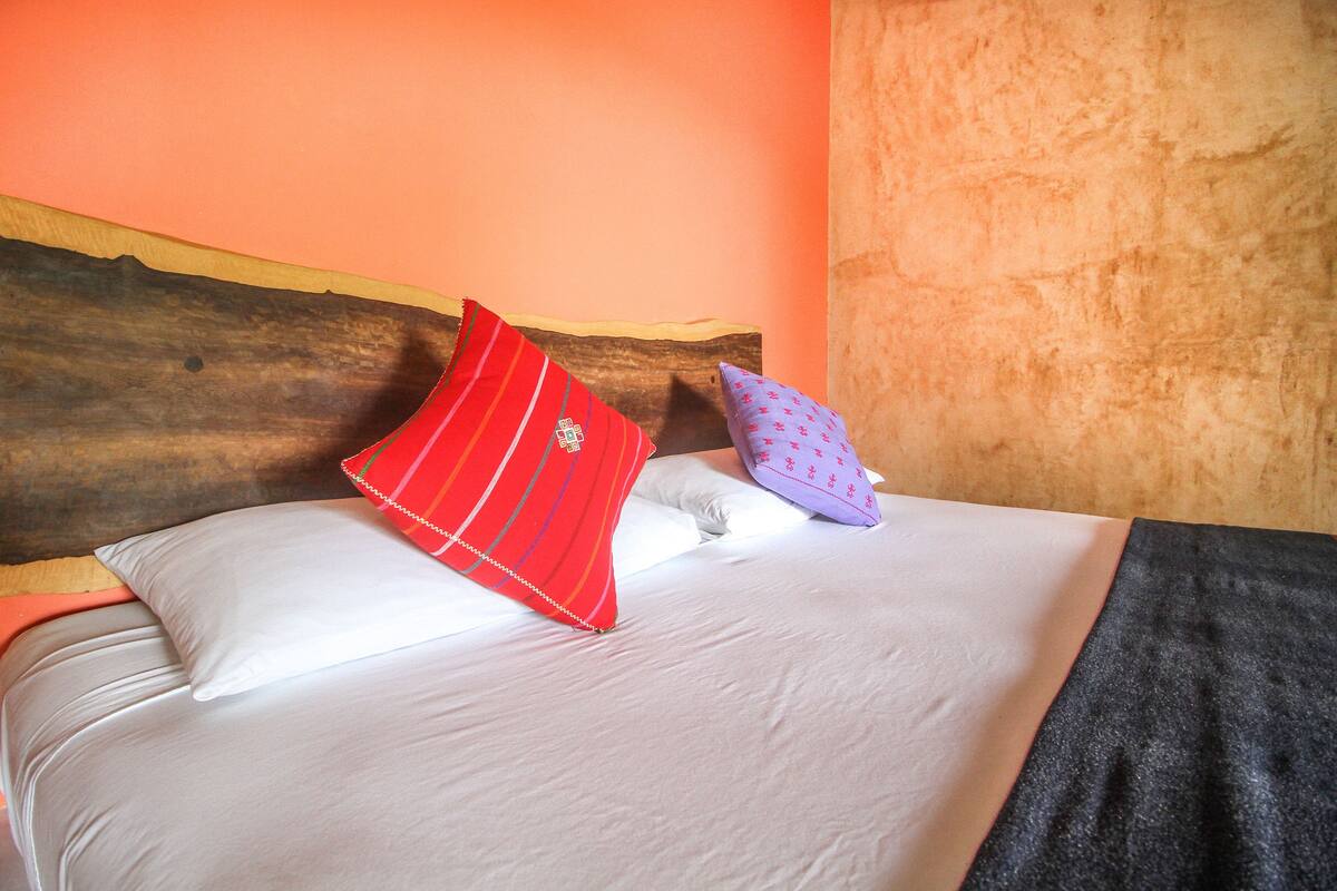 A bed with white bedding, a red striped pillow, and a purple pillow with a pattern.