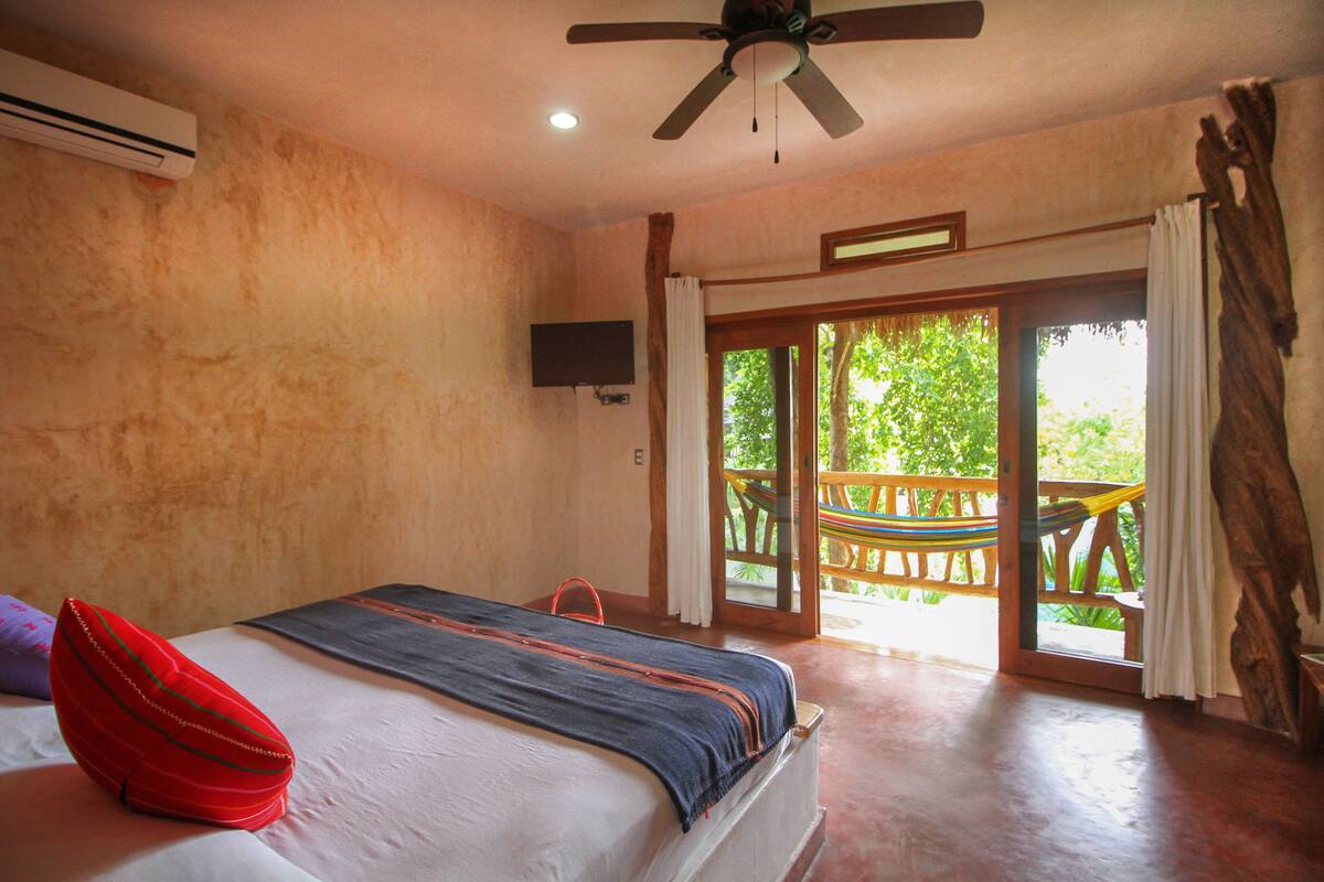 A bedroom with a bed, a ceiling fan, a TV, and a view of the outdoors.
