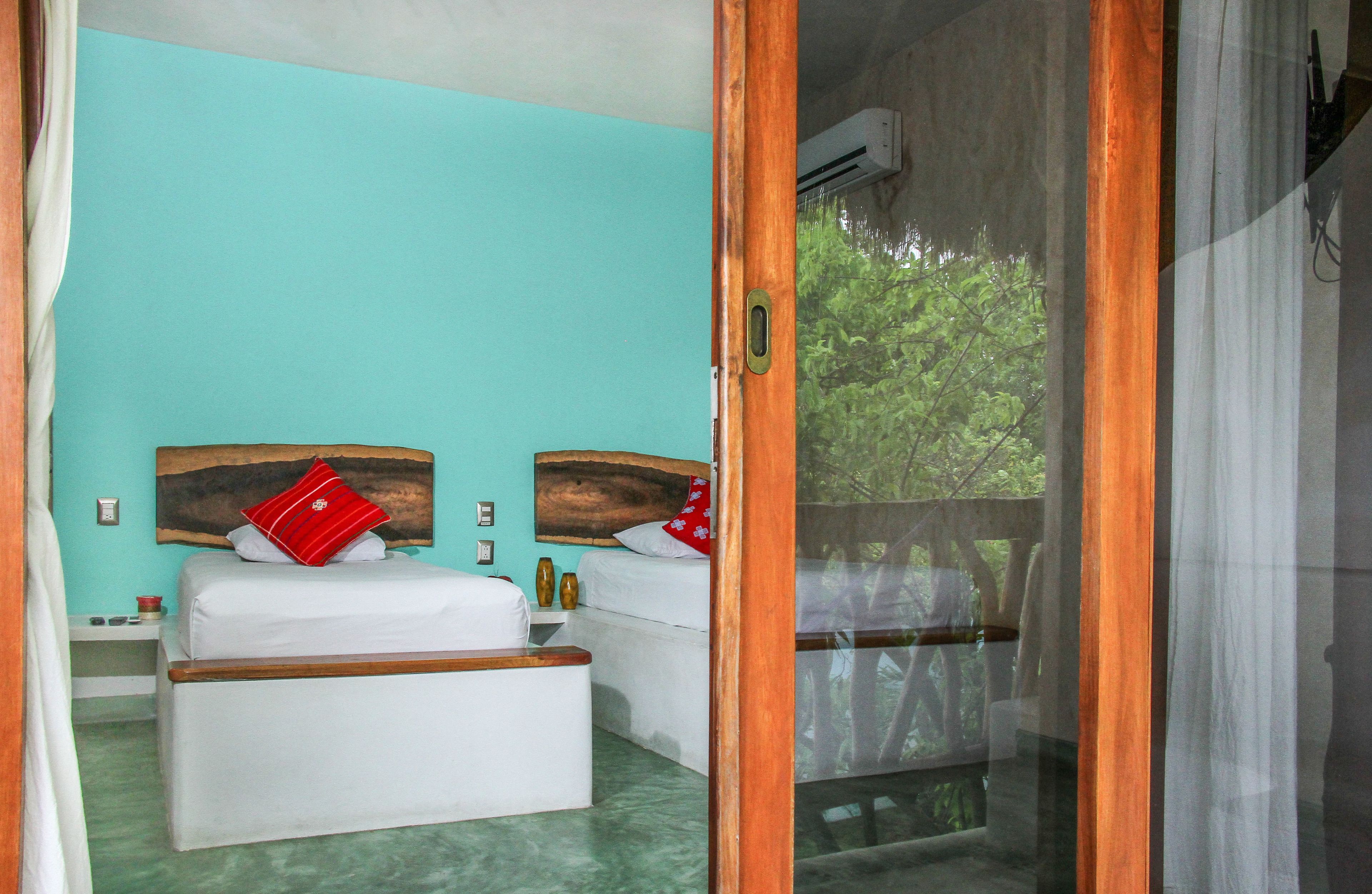 A room with two beds, a wooden headboard, a small table, and a window with a view of trees.