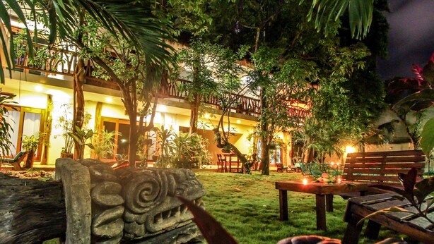 A courtyard with a stone sculpture, outdoor seating, and a building with multiple balconies and warm lighting. - Corazon de Jade Tulum Downtown (Tulum)