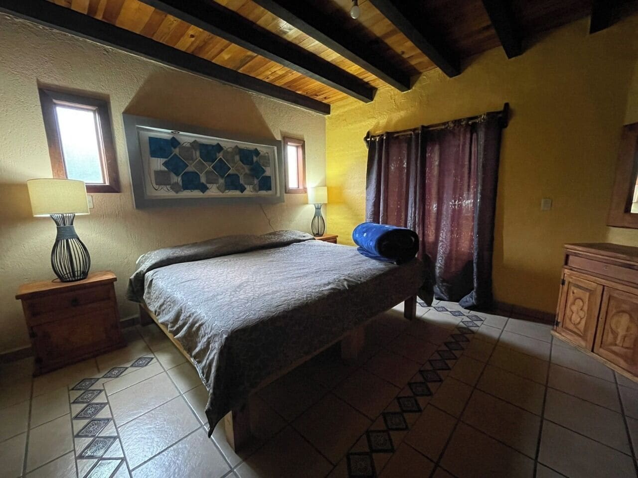A bedroom with a bed, a nightstand, a lamp, a window, and a painting on the wall.